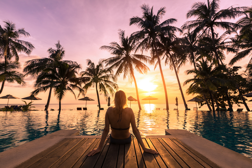 A-woman-relaxes-by-a-pool-on-vacation-in-front-of-a-beautiful-sunset.